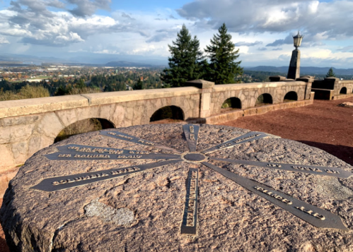 A stone compass rose with directional markers, overlooking a scenic view of a valley and distant mountains.