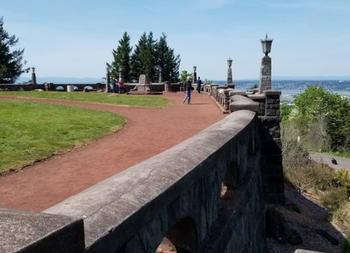 A scenic overlook with a winding path, stone railing, and trees, offering views of the landscape below.
