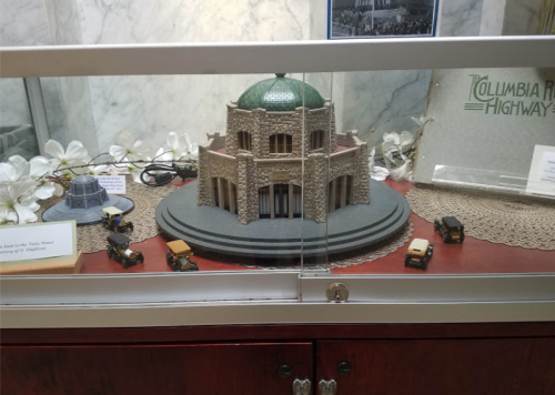 A model of a historic building with a green dome, displayed in a glass case alongside vintage toy cars.