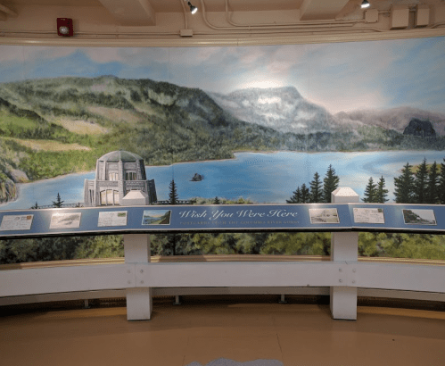 A mural depicting a scenic landscape with mountains, a lake, and a building, accompanied by informational displays.