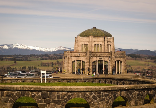 Historic building with a dome, surrounded by mountains and visitors, under a clear blue sky.