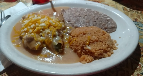 A plate of Mexican food featuring enchiladas, refried beans, and rice topped with cheese.