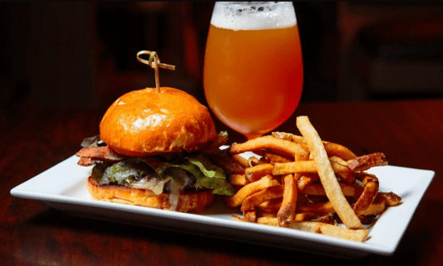A delicious burger with bacon, lettuce, and cheese, served with crispy fries and a glass of beer on the side.