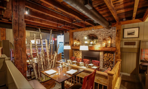 Cozy restaurant interior with wooden beams, a fireplace, and rustic decor, featuring tables set for dining.