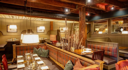Cozy restaurant interior with wooden beams, plaid seating, and elegant table settings under warm lighting.