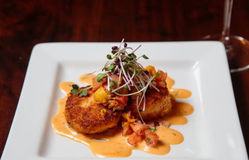 Two golden-brown patties topped with fresh salsa and microgreens, drizzled with a creamy sauce on a white plate.