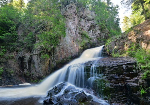 A serene waterfall cascading over rocky terrain, surrounded by lush green trees and cliffs.