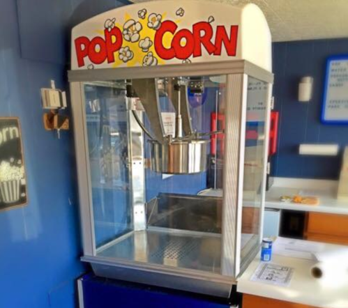 A vintage popcorn machine with a bright "POP CORN" sign, displayed in a blue room.