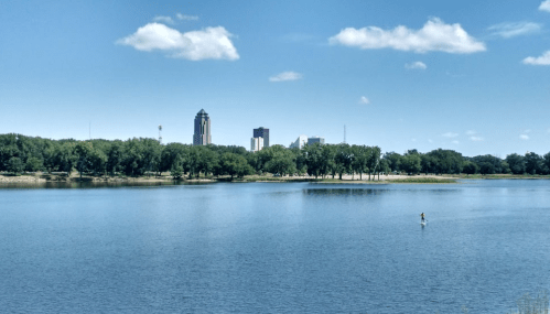 A serene river scene with a person paddleboarding, city skyline in the background under a clear blue sky.