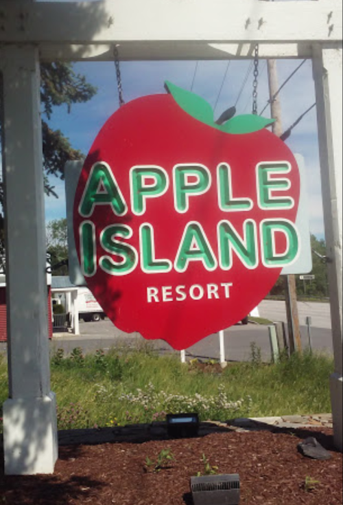 Sign for Apple Island Resort featuring a large red apple design, hanging from a white structure.