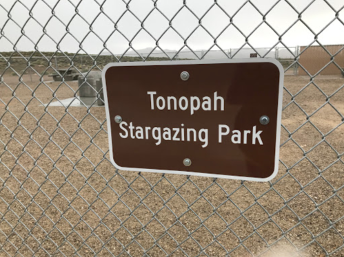 Sign for Tonopah Stargazing Park attached to a chain-link fence, with a gravel area in the background.