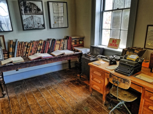 A vintage office with bookshelves, a typewriter, and a "No Smoking" sign near a window.