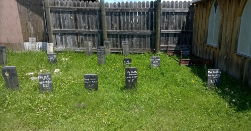 A small graveyard with several tombstones in a grassy area, surrounded by a wooden fence.