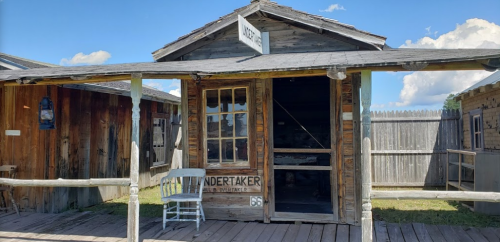 A rustic wooden building labeled "Undertaker" with a rocking chair on the porch and a wooden fence in the background.