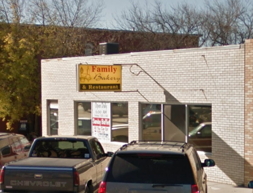 Exterior of a family bakery and restaurant with a sign, featuring parked cars in front and trees in the background.