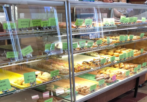 A display case filled with various baked goods, including muffins, pastries, and desserts, each labeled with names.