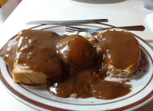 A plate of meat covered in brown gravy, served with mashed potatoes and bread.