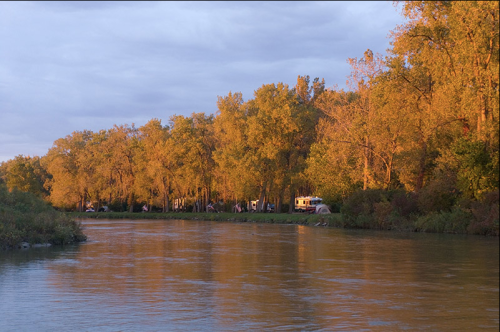 A serene river scene with golden trees reflecting in the water under a cloudy sky at sunset.