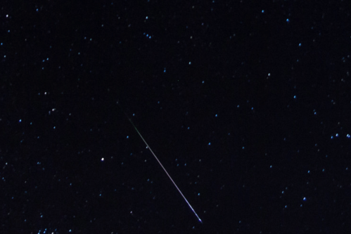 A night sky filled with stars, featuring a bright meteor streaking across the scene.