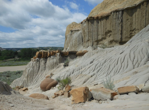 A rugged landscape featuring layered rock formations and smooth, flowing textures under a cloudy sky.