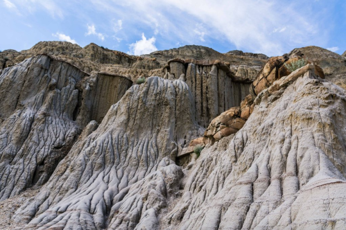 A rugged, textured rock formation with layered cliffs under a blue sky, showcasing natural erosion patterns.