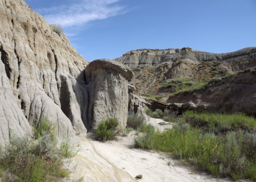 A rocky landscape with unique formations, green grass, and a clear blue sky in the background.