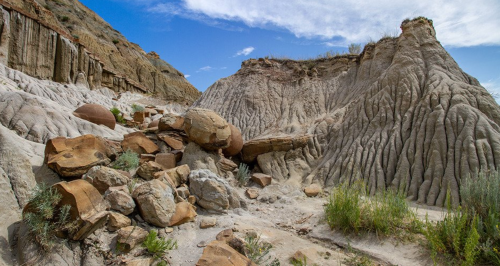 A rugged landscape featuring textured rock formations and scattered boulders under a blue sky with wispy clouds.