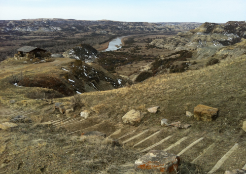 A scenic view of a river winding through hills, with a small cabin and rocky terrain in the foreground.