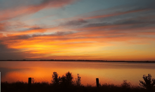 A serene sunset over a calm lake, with vibrant orange and pink clouds reflecting on the water's surface.
