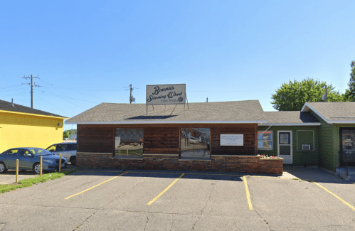 A small, rustic building with a sign reading "Bonnie's Sausage World," surrounded by parked cars and clear blue skies.