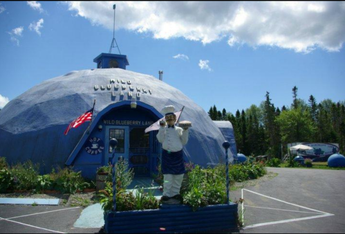 A blue dome-shaped building with a chef statue holding a pie in front, surrounded by trees and a clear blue sky.