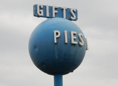 A blue spherical sign with the words "Gifts" and "Pies" in white letters against a cloudy sky.