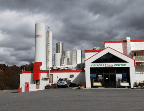 A visitors center building with silos in the background, under a cloudy sky. A car is parked in front.