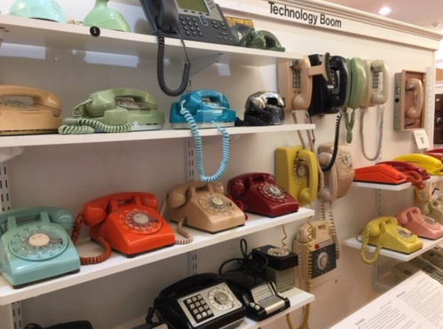A colorful display of vintage telephones on shelves, showcasing various styles and colors from different eras.