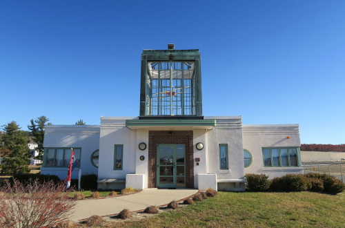 A modernist building with a glass tower, surrounded by greenery and a clear blue sky.