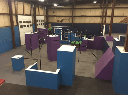A colorful indoor obstacle course with various geometric shapes and climbing structures in a spacious gym.