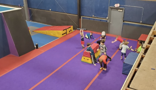 A colorful gym with children practicing gymnastics on mats and equipment, engaging in various activities.