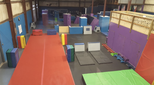 A spacious indoor gym with colorful obstacle course equipment and mats arranged for training and activities.
