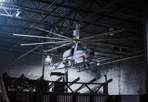 A large helicopter model hangs from the ceiling of an industrial space, with a shark mouth design on its nose.
