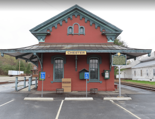 Historic red train station with green accents, featuring a sign that reads "Chester" and accessible parking spaces.