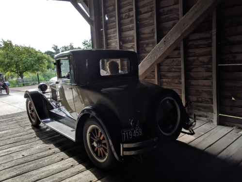 A vintage car parked inside a rustic wooden barn, with sunlight filtering through the open door.