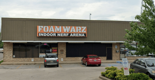 Exterior of Foam Warz Indoor Nerf Arena, featuring a brick facade and parking lot with cars.