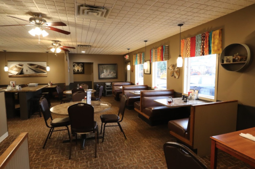 Cozy diner interior with booths, tables, and colorful window treatments, featuring warm lighting and a welcoming atmosphere.