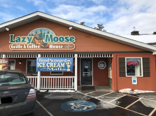 Exterior of Lazy Moose Grille & Coffee House, featuring a sign for ice cream and an "Open" banner. Snow on the ground.