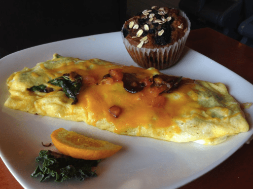 A plate with a cheese omelet topped with vegetables, an orange slice, and a muffin with oats and berries.