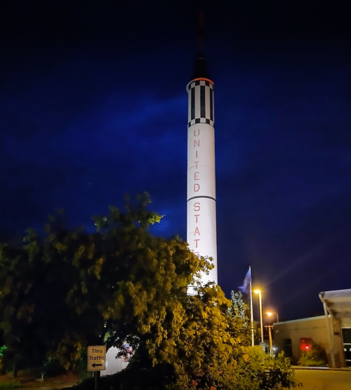 A tall rocket monument with "UNITED STATES" written on it, illuminated at night against a dark sky.