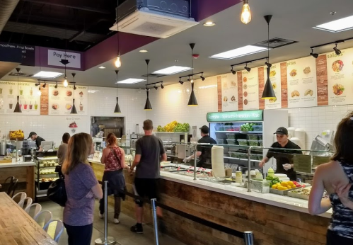 A busy smoothie bar with customers ordering at the counter, surrounded by fresh fruits and menu boards.
