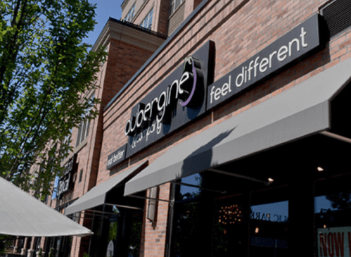 Exterior of a restaurant named "Aubergine," featuring a modern sign and awnings, surrounded by trees.