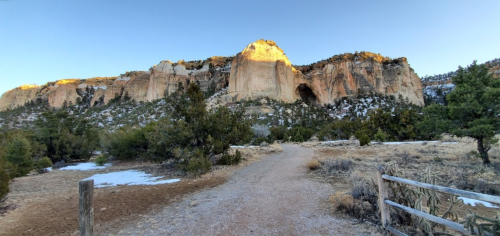 A scenic view of a rocky cliff at sunrise, with a dirt path and sparse vegetation in the foreground.