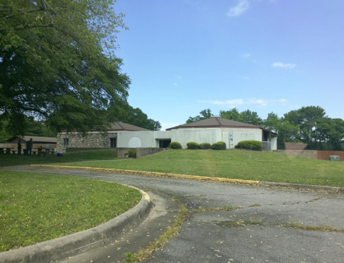 A grassy area with a curved driveway leading to a low, modern building under a clear blue sky.